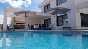 Un área de piscina moderna con agua azul cristalina, sillas de descanso y sombrillas.