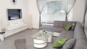 Una sala de estar moderna con un sofá gris, una mesa de centro de vidrio y un televisor de pantalla plana montado en la pared.