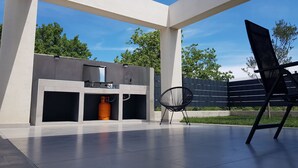 Un patio exterior con una moderna zona de barbacoa, una silla y una valla de fondo.