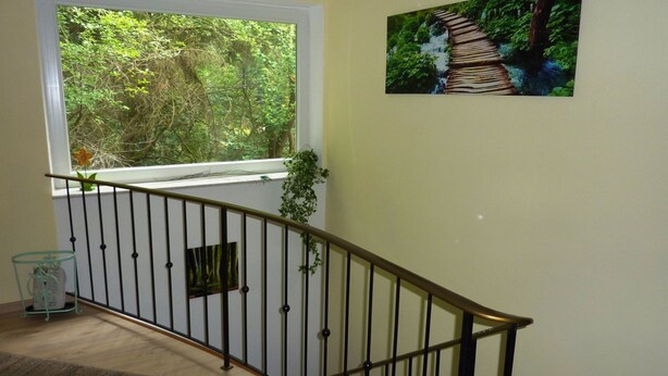 Una escalera con barandilla metálica, una ventana con vistas a zonas verdes, y un cuadro con motivo de un bosque en la pared.