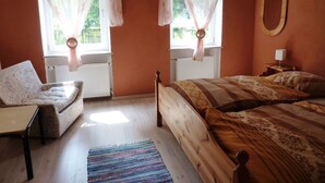 Un dormitorio con cama, una silla, una ventana con cortinas, un radiador y un espejo en la pared.