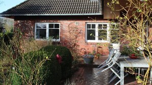 A brick house with a tiled roof, two windows, a patio with a table and chairs, and a small garden area. - Lüntjenüst by Interhome (Marienhafe)