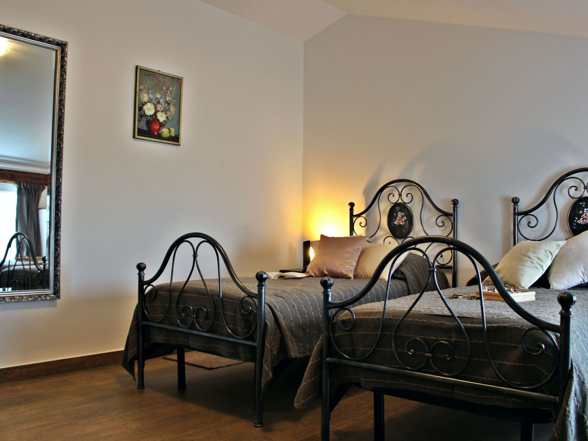 Un dormitorio con dos camas metálicas, una mesita de noche, un espejo y un cuadro en la pared.