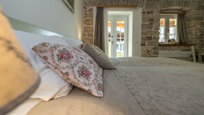 A bedroom with a stone wall, a bed with floral pillows, a wooden headboard, and a view through a doorway. - VILLA CON WELLNESS A 1 KM DAL MARE by Interhome (Umag/Juricani)