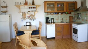 Eine kompakte Küche mit Holzschränken, einem weißen Kühlschrank, einem Esstisch mit Stühlen und einer gefliesten Spritzschutzwand.