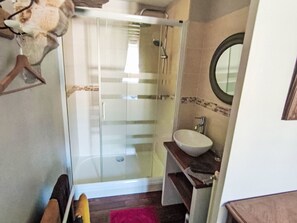 Ein Badezimmer mit Glasdusche, Waschbecken mit Spiegel und einer Holzbank.