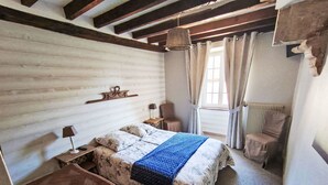 Et soveværelse med en træseng, et natbord, en stol, et vindue med gardiner og en radiator.