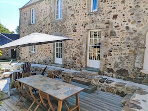 Un bâtiment en pierre doté d’un patio comprenant une table, des chaises et un parasol.