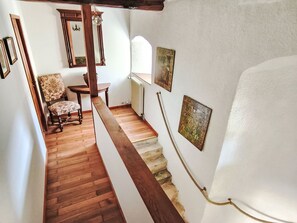Un escalier avec des rampes en bois, une chaise recouverte d’un tissu à motifs floraux et des œuvres d’art encadrées accrochées aux murs.