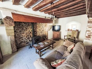 Un salon de style rustique avec des poutres apparentes, un mur en pierre, une cheminée, un téléviseur et un canapé.