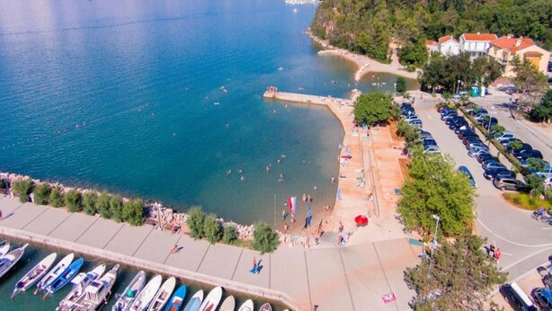 Ett område vid kusten med en småbåtshamn, en strand och bostadshus.