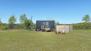 A small, dark-colored cabin with a porch and outdoor seating, surrounded by a grassy field and trees. - A perfect escape for couples seeking comfort, privacy, and scenic simplicity. (Temple Bruer)