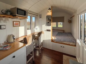 A compact, well-lit room with a kitchenette, a bed with a patterned bedspread, and a window providing a view of the outdoors.