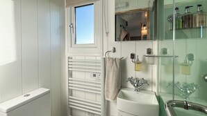 Un baño con inodoro blanco, cabina de ducha de vidrio, lavamanos blanco y una toalla colgada en un perchero.