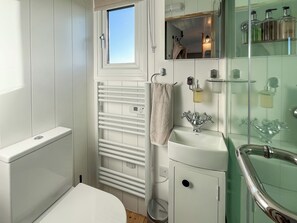 A bathroom with a white toilet, a glass shower enclosure, a white sink, and a towel hanging on a rack.