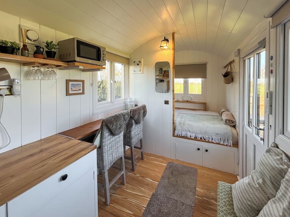 A compact room with a kitchenette, a bed with a window, a small table, and a chair.