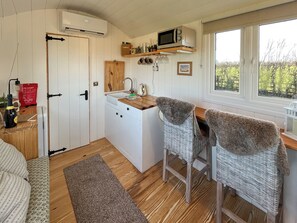 A compact kitchen with a microwave, sink, and wooden cabinets. There are two wicker chairs with grey throws.