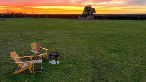 A grassy outdoor area with a barbecue grill and Adirondack chairs. - A perfect escape for couples seeking comfort, privacy, and scenic simplicity. (Temple Bruer)