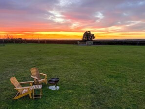 Een gazon met een barbecue en Adirondack-stoelen.