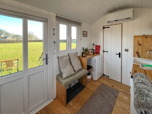 A compact room with a bench, a small table, a door, and a view of a green field.