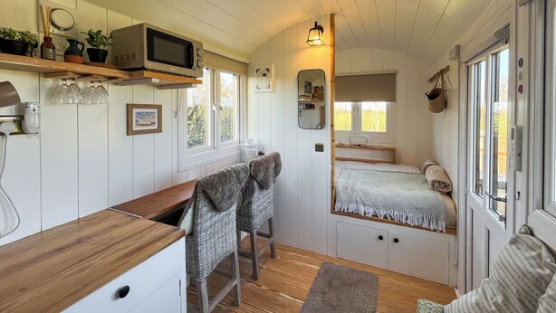 Una habitación compacta con kitchenette, cama con ventana, pequeña mesa y una silla.