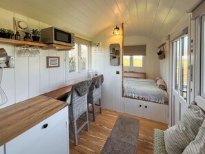 A compact room with a kitchenette, a bed with a window, a small table, and a chair.