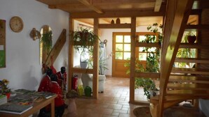 Un intérieur en bois avec un escalier, une table avec des livres et des plantes en pot.