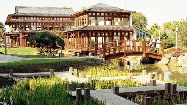 Il s'agit d'un bâtiment de style japonais traditionnel, doté d'une structure en bois, d'un pont enjambant un étang et d'un jardin bien entretenu avec une terrasse en bois.