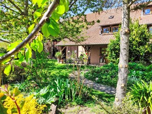 Ein Garten mit einer Holzkonstruktion, einem Baum und einem Gebäude mit Ziegeldach.