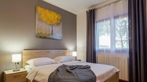 Un dormitorio con una cama de madera, dos mesitas de noche, una lámpara de noche, un cuadro en la pared y una ventana con cortinas.