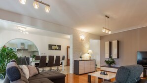 Una sala moderna con un sofá, un comedor con sillas y una mesa, una cocina al fondo y un televisor sobre un mueble.