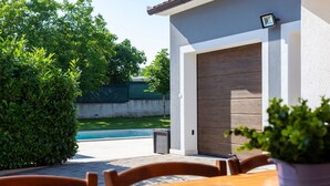 Un patio con una mesa y sillas de madera, una pequeña planta en maceta y vistas a una piscina y follaje.
