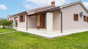 Una casa a un piano con un portico coperto, un camino e un piccolo giardino.