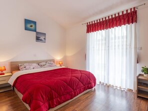 A bedroom with a large bed, two bedside lamps, a window with sheer curtains, and a red valance. - "Villa Mirela" mit Terrasse by Interhome (Barban)