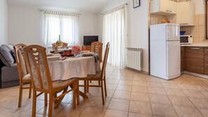 Una cucina moderna con frigorifero, microonde e forno bianchi. C'è un tavolo da pranzo con sedie e una TV sullo sfondo.