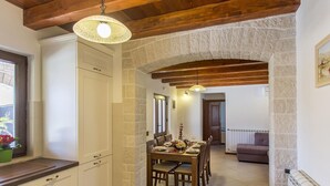 A dining area with a stone archway, wooden ceiling beams, white cabinets, and a dining table set for six. - Casa Mia mit privatem Pool by Interhome (Barban)