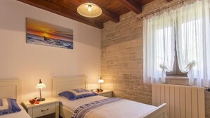 A bedroom with two beds, a stone wall, a window with sheer curtains, and a painting of a sunset. - Casa Mia mit privatem Pool by Interhome (Barban)
