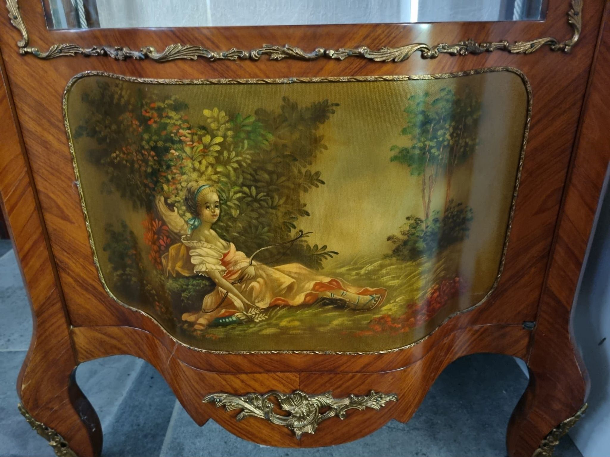 A wooden cabinet with a glass top, featuring a painted landscape scene.