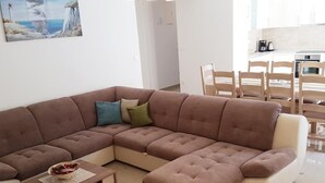 Ein modernes Wohnzimmer mit einem Ecksofa, einem kleinen Holztisch und einem Essbereich mit Holzkästen.