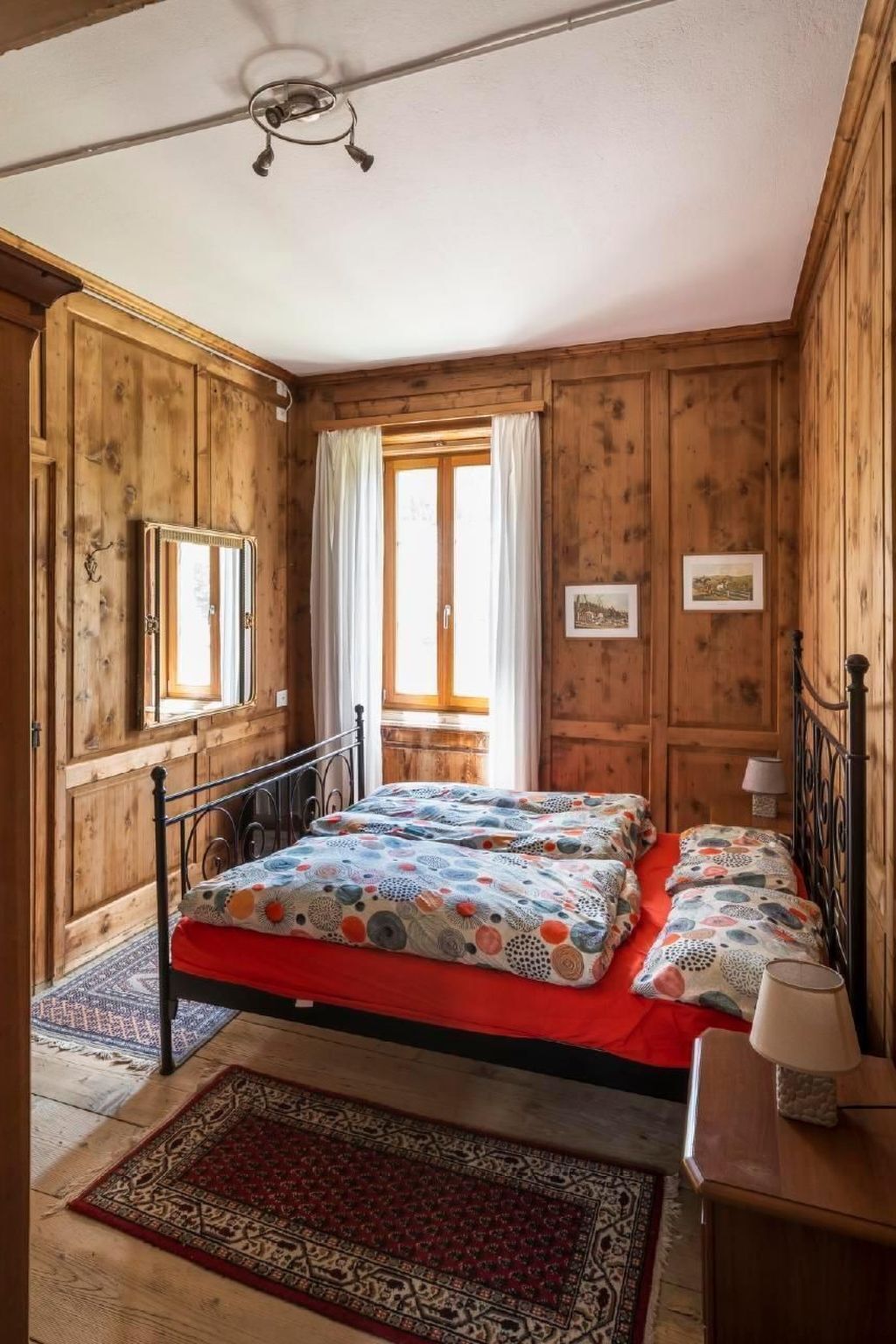 A wooden room with a bed, a small table, and a chair.