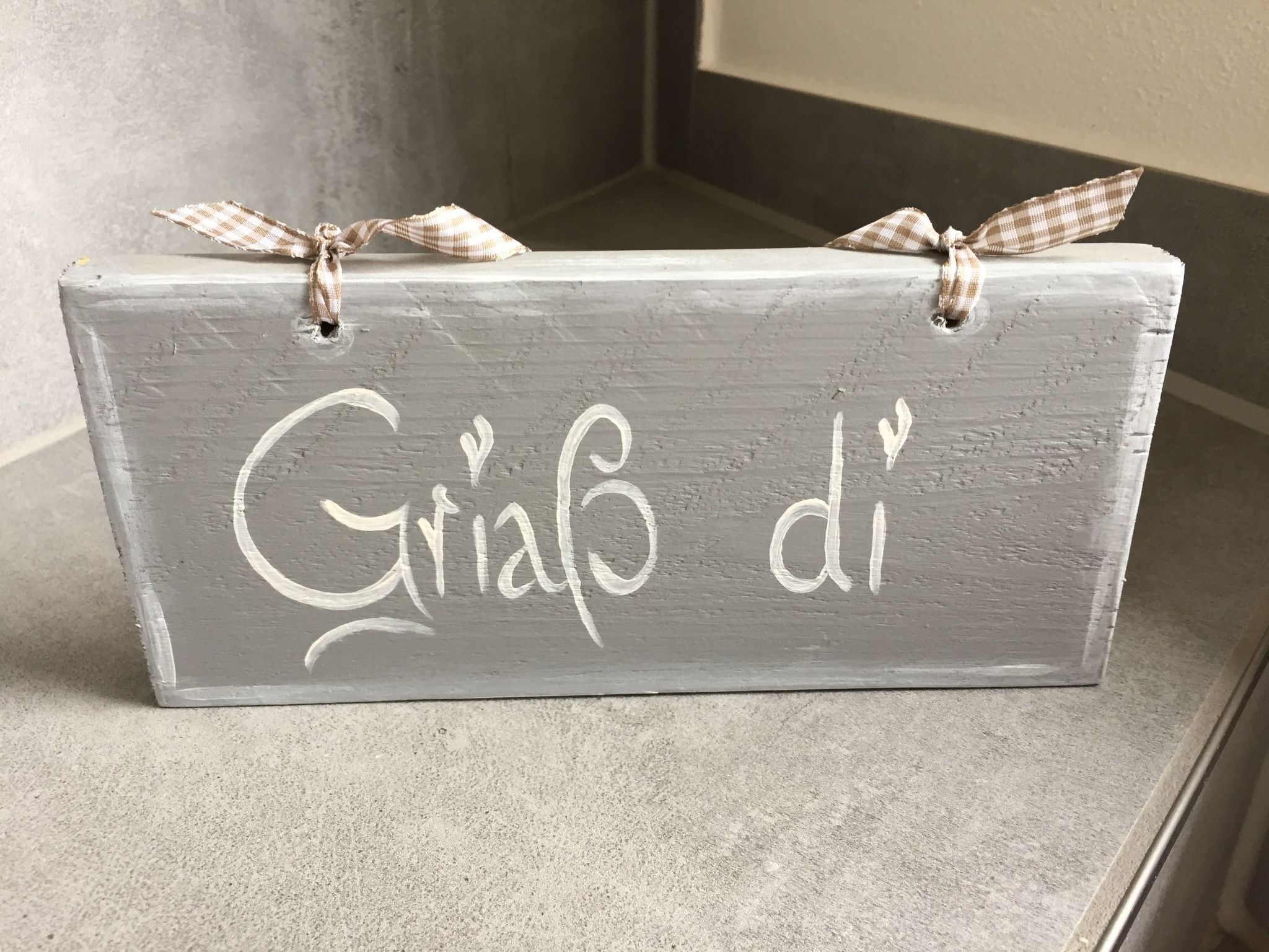 A rectangular wooden sign with the text "Giacob' di" written on it, tied with a checkered ribbon.