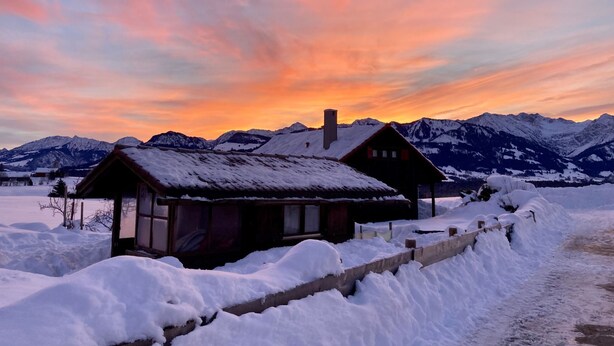 A cabin with a snow-covered roof and a chimney, surrounded by a snowy landscape and mountains in the background. - Fewo Bergblick lodge by Interhome (Ofterschwang)