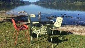 A lakeside table with chairs and a sign, surrounded by grassy banks and a calm lake with hills in the background. - Fewo Bergblick lodge by Interhome (Ofterschwang)