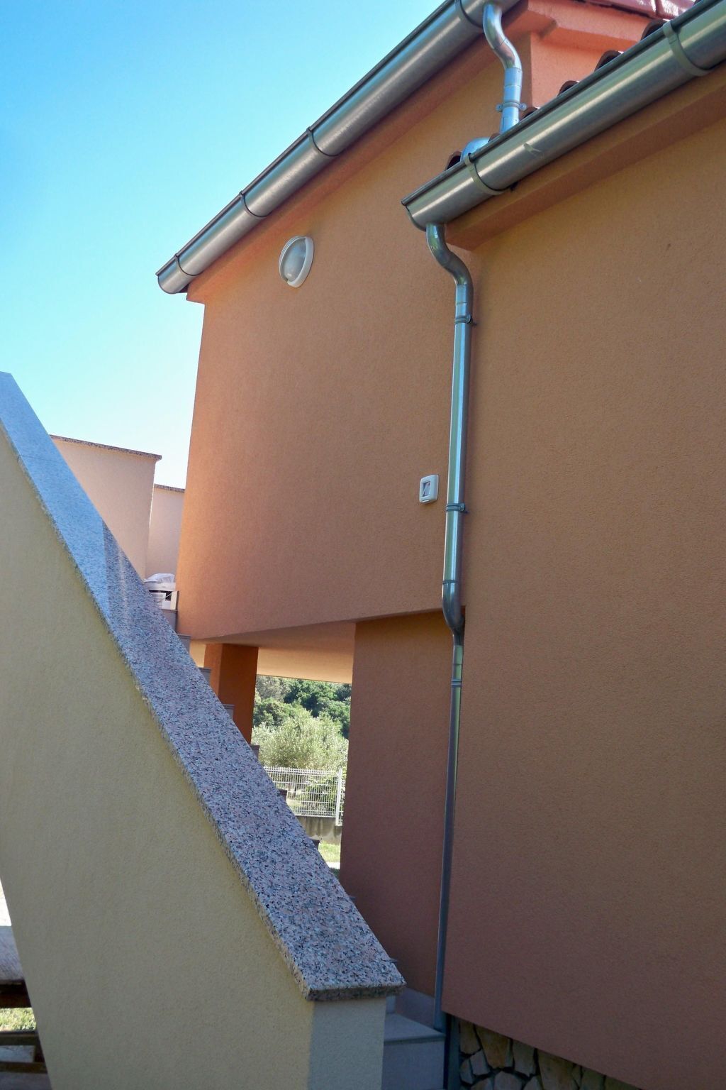 Un coin d’immeuble avec une façade de couleur beige, une gouttière en métal et une petite fenêtre.
