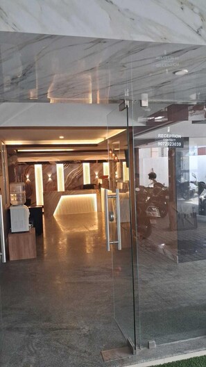 A reception area with a marble floor and glass doors, a reception desk, and a motorcycle parked outside. - Celestial Heights (Kanayannur)