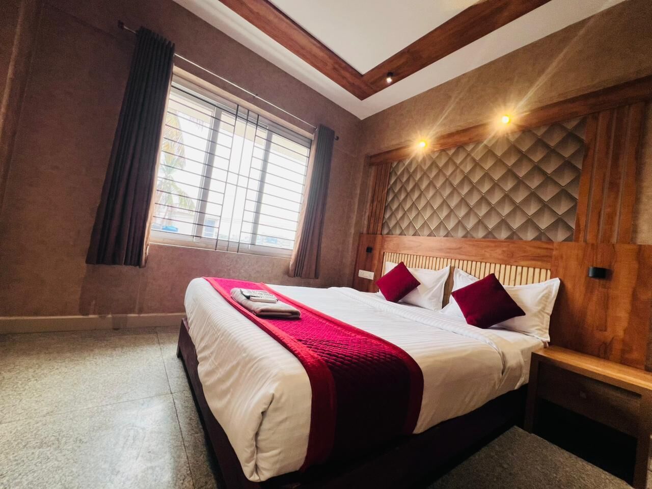 Una habitación de hotel con una cama grande, cabecera de madera y una ventana con cortinas.