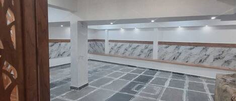 A spacious room with a tiled floor, a marble wall, and recessed ceiling lights.
