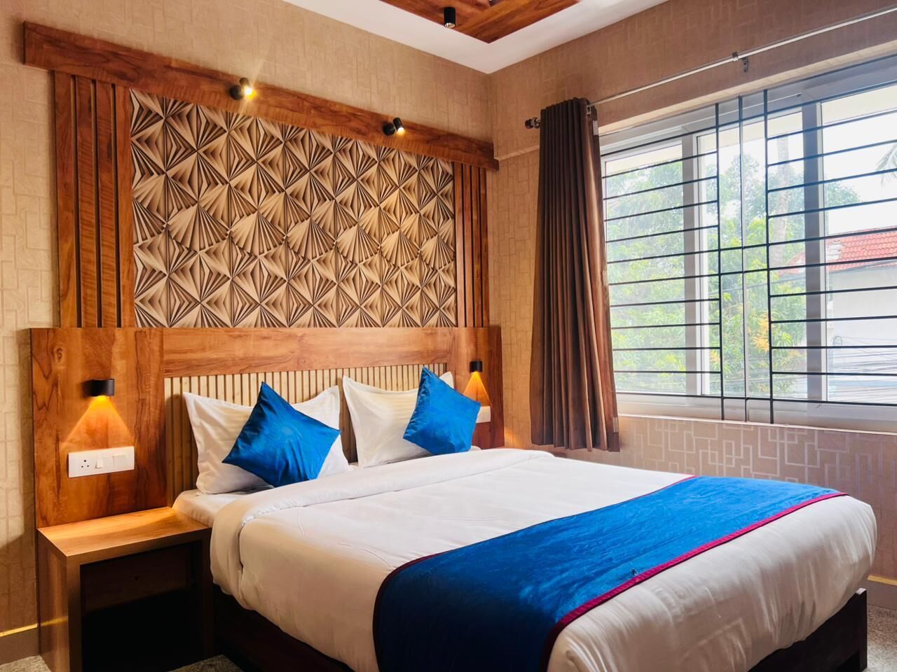 A hotel room with a large bed, wooden headboard, and a geometric-patterned wall panel.