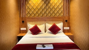 A hotel room with a bed, wooden headboard, two bedside tables, and a ceiling fan. - Celestial Heights (Kanayannur)