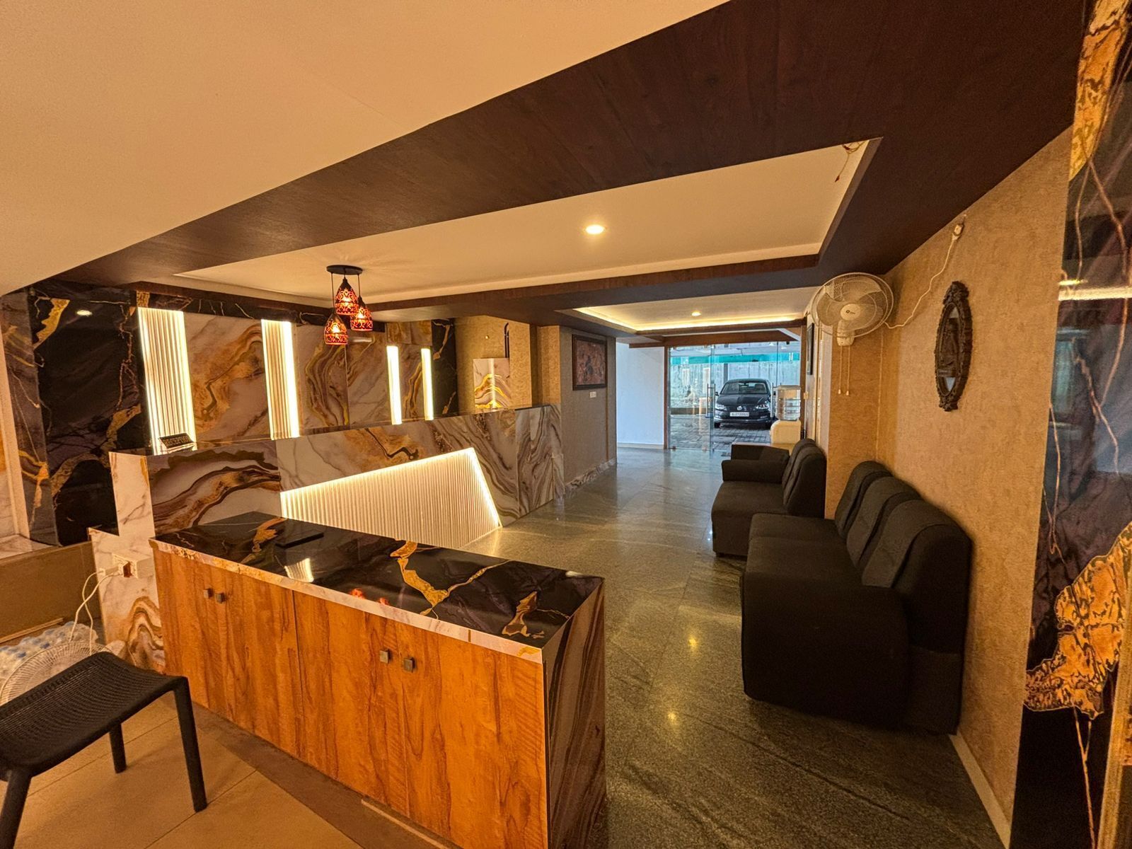 Un hall d’entrée moderne avec un comptoir de réception en marbre, un meuble en bois, un canapé en cuir noir et un ventilateur de plafond.